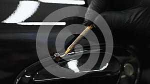 Close-up shot of a black car part being painted with a fine fluid pen