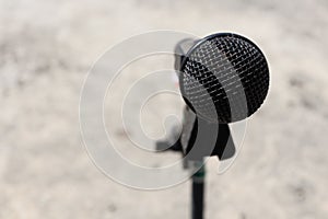 Close-up shot of a black microphone mounted on a metal stand, placed outdoors, selectable focus, blurred background.