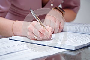 Close up shot of bride signing up the festive wedding document of marriage registration, only hands with ring, pen visible