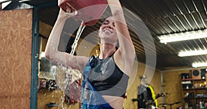 Close-up shot of a brunette mechanic girl in a black top dousing herself with a canister of water against of her garage