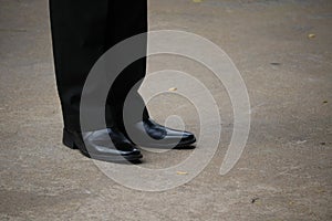 Close-up shot of a business man wearing slacks and black leather shoes standing on a cement floor, outdoor street, optional focus.