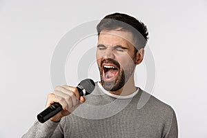 Close-up shot carefree cheerful gay man with beard, grey sweater, singing along upbeat song, holding microphone, carried