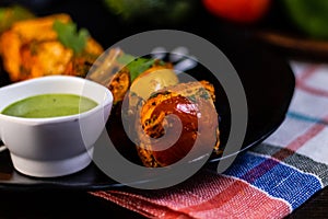 Close up shot of Cheese Tikka with green spicy sauce in garnish plate kept on chequered table cloth