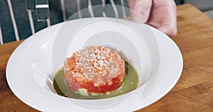 Close-up shot of chef's hands in gloves preparing delicious salmon and tomato salad with green sauce and sesame seeds in