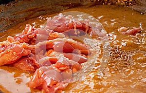 Close up shot of chicken meat being added to a creamy Thai red curry dish.