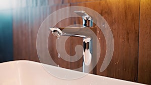 close-up shot chrome plated trendy leaking faucet water dripping into sink, broken leaking plumbing tap. drops of water