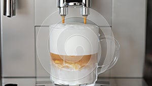 Close up shot of coffee pouring into glass cup with milk, making cappuccino using the automatic coffee machine. Beverage