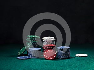 Close-up shot of a colorful chips piles, some of them laying nearby on green cover of playing table. Black background