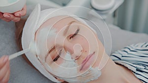 Close-up shot of Cosmetician hands applying cream mask on young woman`s face at beauty spa salon