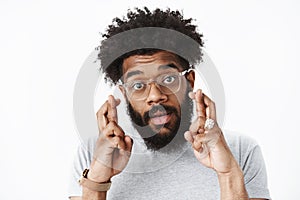 Close-up shot of cute african american adult bearded guy with afro hairstyle and pierced nose in glasses crossing hands