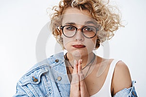 Close-up shot of cute pouting girl begging for favour, making silly face being in need holding hands in pray while