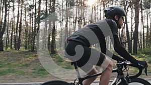 Close up shot of cyclist pedaling bike wearing black jersey, shorts, helmet and sunglasses. Back road carbon bicycle in the park.