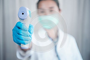 Close-up shot of doctor wearing protective surgical mask ready to use infrared forehead thermometer to check body temperature for