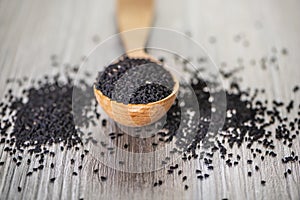 Close up shot of dried seeds of black cumin seeds kalinji on wooden spoon on rustic wooden background. Soft focus