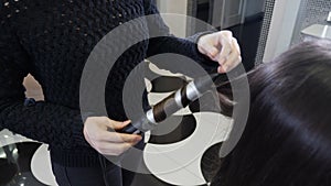 Close-up shot of female hairstylist curling hair using hair iron. Process of curling long hair with hair tongs in modern