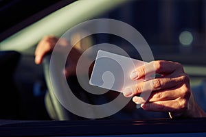 Close up shot of a female hand holding blank plastic card, woman sitting in car and showing driver license