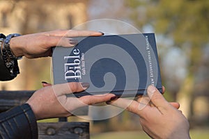 Close up shot of female hands and a male hand holding the Bible on a blurred background