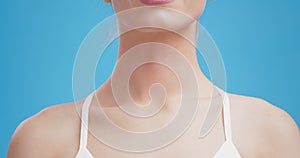 Close up shot of female neck with red pulsating inflamed spot, sore throat illness, blue studio background