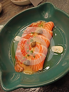 Close up shot of fresh salmon carpaccio glazed in olive oil on a green small ceramic bowl
