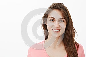 Close-up shot of friendly communicative woman in pink t-shirt, smiling joyfully and gazing with care and warm expression