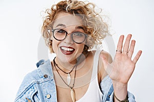 Close-up shot of friendly outgoing, sociable stylish european female newbie in glasses with short blond curly hair