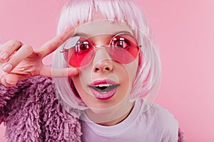 Close-up shot of funny european girl in colorful periwig and pink sunglasses. Indoor photo of attra