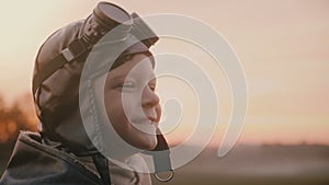 Close-up shot of funny little boy in old pilot costume with scarf and glasses making silly faces in a field slow motion.