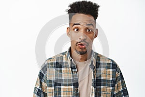 Close up shot of funny and silly african american guy with curly afro hair, squinting, pucker lips, mimicking, standing