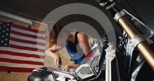 close-up shot: a girl auto mechanic repairs a motorcycle in her workshop with a screwdriver against the background of