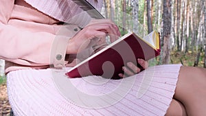 Close-up shot of a girl in the autumn forest, a female hand writes with a pen in a book. A woman sits near a tree in the