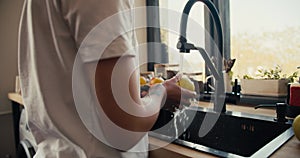 Close-up shot of a girl in a white T-shirt washes fruit in the sink in the kitchen. Healthy eating fruits as part of