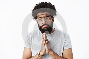 Close-up shot of gloomy and silly african american bearded boyfriend with pierced nose holding hands in pray making