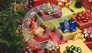 Close up shot of glossy red sphere ball hanging decorating on Christmas pine tree branch in front lot of Xmas eve wrapped present