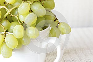Close up shot of green grapes in a white cup on white background.