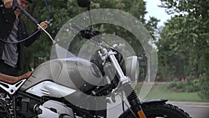 Close-up shot of guy washing scrambler motorbike with water hose