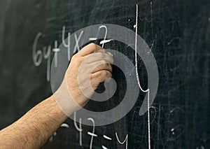 Close-up shot of a hand holding chalk and writing mathematical equations on the blackboard