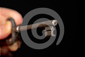 Close-up shot of a hand holding a silver key against a black background