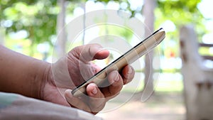 Close up shot hand of man using mobile smart phone in nature public park with ambient sound