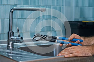 Close up shot of hand of professional repairman holding a pipe wrench while fixing faucet in the kitchen