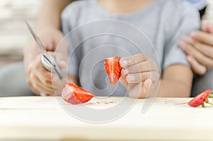 Close up shot hands of girl cutting straberry on wooden cutting