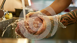 Close up shot of hands of male cook wearing protective gloves rinsing raw pork meat under tap water for cooking