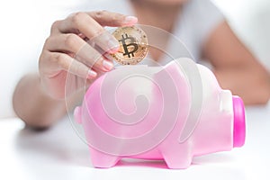 Close up shot hands of woman putting gold bitcoin to pink piggy