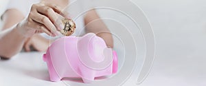 Close up shot hands of woman putting gold bitcoin to pink piggy