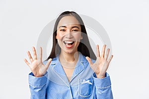 Close-up shot of happy attractive asian woman in blue pyjama showing ten fingers and smiling white teeth, explain main