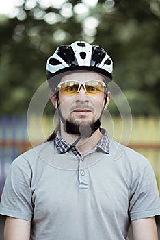 Close up shot of happy attractive young man with beard wearing protective helmet and yellow sunglasses looking at camera