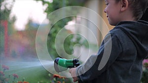 Close-up shot of a happy little boy watering flowers with a spray gun. The child smiles, the concept of children`s