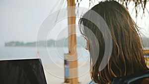 Close-up shot of happy successful businesswoman working on laptop mobile office online in swimsuit on exotic sea beach.