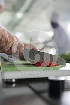 Close up shot of head chef hands cutting fresh and organic red bell pepper while cooking gourmet dish