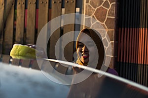 Close up shot hijab woman washing car roof with a smile