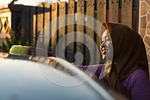 Close up shot hijab woman washing car roof with a smile